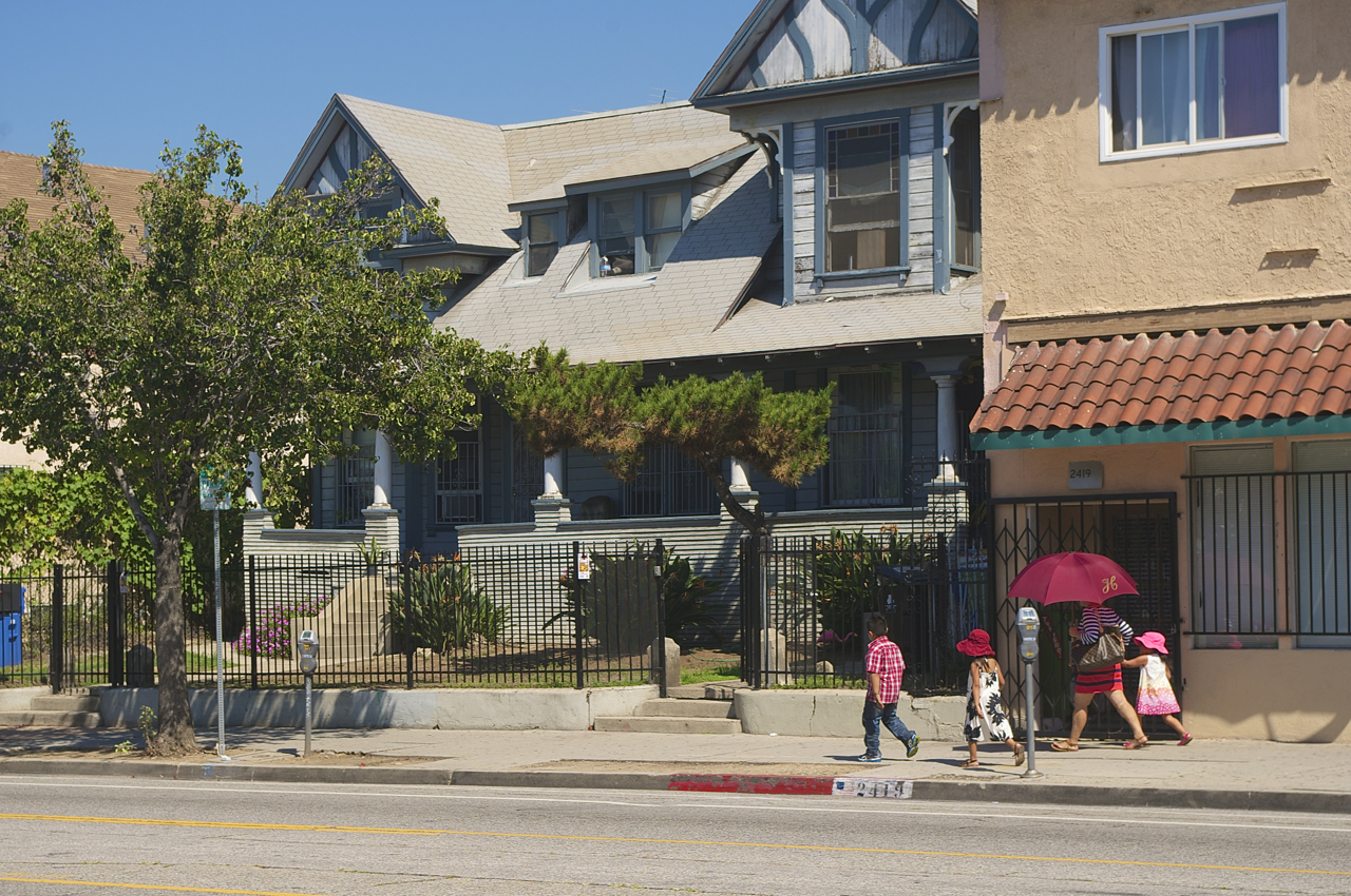 A woman walks toward Soto St. with her children. The girls have hats and she has an umbrella. Sahra Sulaiman/Streetsblog L.A.